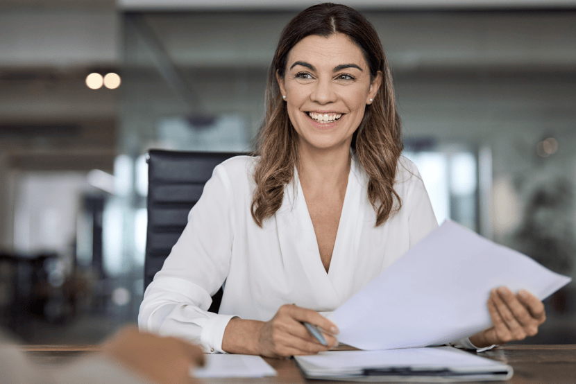 Smiling woman holding papers in front of an office background